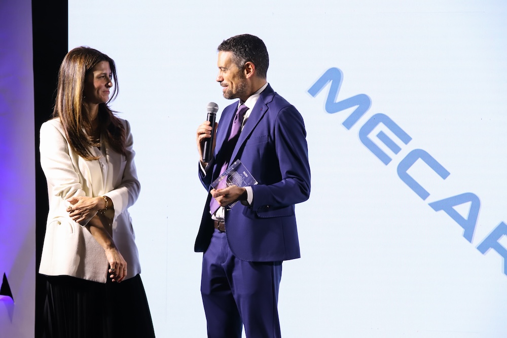 La consegna di un riconoscimento sul palco, davanti al logo Mecar